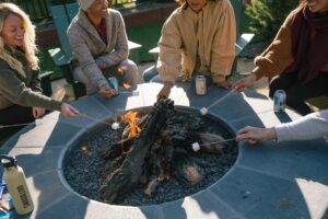 Guests roasting marshmallows for s'mores at the fire pit outside Station House Inn in the evening.
