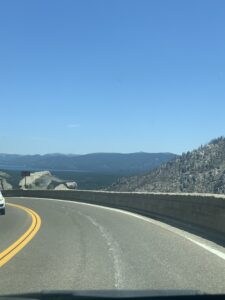 Two-lane mountain highway winding along Echo Summit, with a first glimpse of Lake Tahoe's blue water in the distance on the drive from the Bay Area.